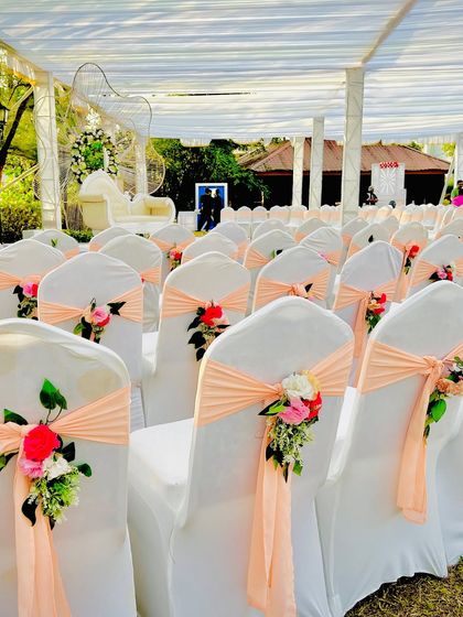 Elegant guest seating for a daytime ceremony. The white chairs are decorated with peach-colored sashes and small floral bouquets, adding a touch of color and sophistication.