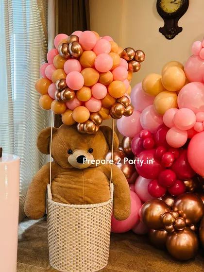 A close-up look at a creative and whimsical hot air balloon prop, featuring a large teddy bear in a woven basket. The balloon is crafted from a dense cluster of pink, peach, and chrome gold balloons, showcasing my attention to detail.