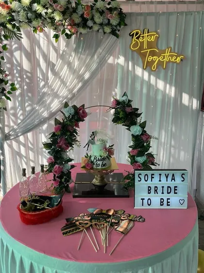 A complete bridal shower setup featuring a cake table, fun props, and a personalized light-box sign. The backdrop includes a floral arch and a "Better Together" neon sign.