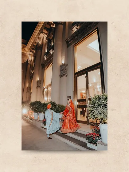 The groom helps his bride down the stairs of the grand venue, a chivalrous and romantic moment captured at night.