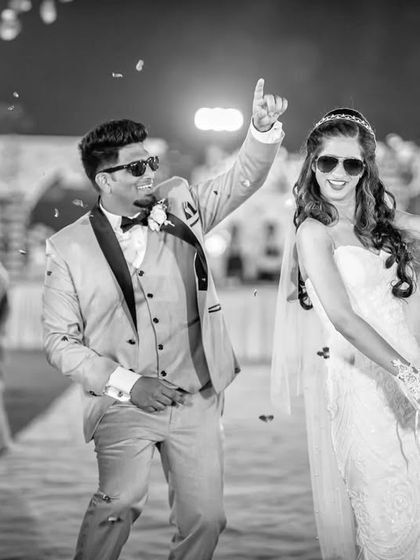 The couple dancing down the aisle during their reception entrance, showered with confetti. This black and white candid is full of motion and joy.