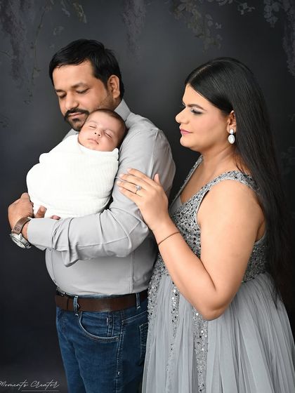 A classic portrait of a new family. The parents look lovingly at their sleeping newborn, creating a peaceful and timeless image against a simple, dark background.