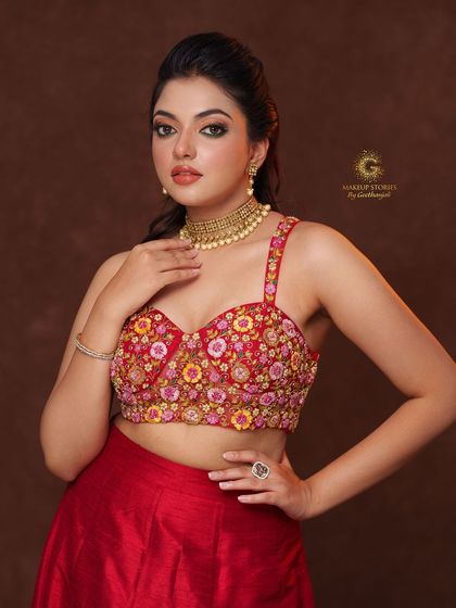 A modern lehenga look featuring a red bustier-style crop top with vibrant multi-color floral embroidery, paired with a simple red skirt.