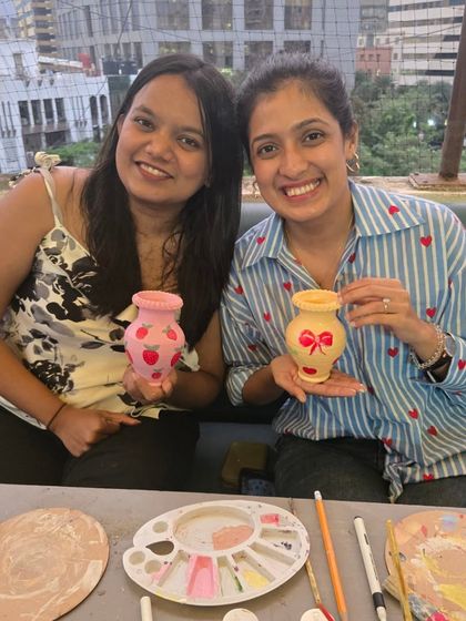 Two participants happily show off the matching vases they've just painted, one with strawberries and the other with a bow.