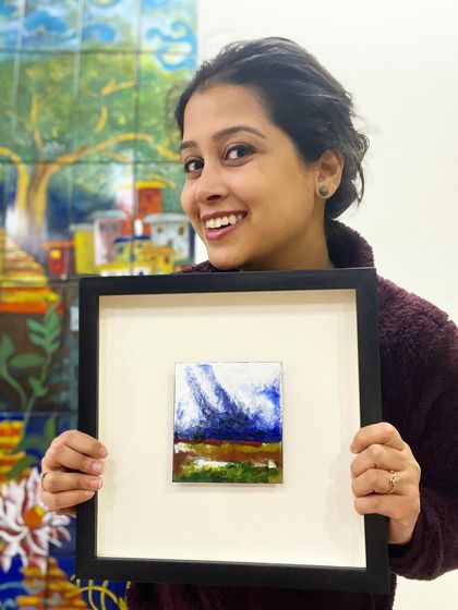 Me holding a framed miniature landscape I created with enamel on copper. We also create and sell original art for your home or as a unique gift.