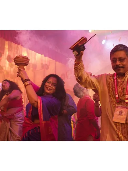 A couple dances with joy during the evening celebrations, one holding a dhunuchi and the other a traditional Bengali incense burner.