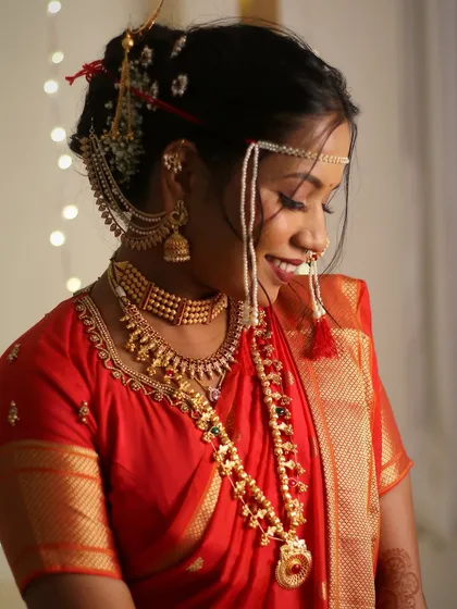 This candid shot captures the bride's shy smile and the intricate details of her bridal jewellery and makeup. The red saree look is a timeless choice for Maharashtrian weddings.