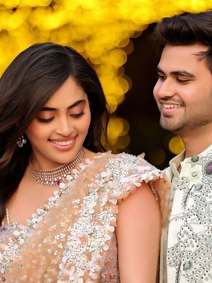 A beautifully lit evening shot of a couple, with the soft glow of bokeh lights in the background. This portrait captures a quiet, happy moment between them during their celebration.