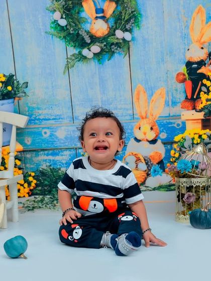 This little guy is all smiles in our rabbit-themed first birthday setup. The cheerful blue background and playful props create a happy atmosphere for this milestone celebration.