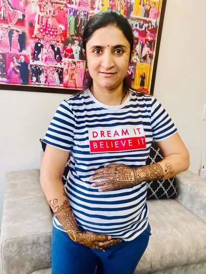 A lovely portrait of a client celebrating her pregnancy with a custom maternity mehndi. Her shirt says 'Dream It Believe It', perfectly matching the joyful occasion.