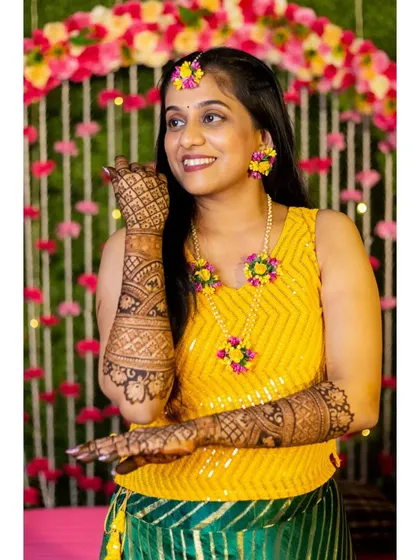 A beautiful portrait of the bride in her yellow mehendi outfit and floral jewelry, displaying her gorgeous henna.