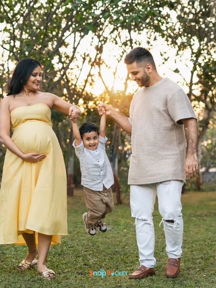 A fun-filled outdoor maternity session in a sunlit garden. The family plays together, swinging their son, showcasing a candid and joyful approach to capturing this special time.