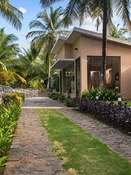 A pathway lined with lush greenery leads to the resort villas, which are nestled among palm trees. The image conveys a sense of being immersed in a tropical, natural environment.
