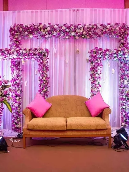 A beautiful stage backdrop framed with purple orchids and other flowers. The purple uplighting and white drapes create a vibrant yet elegant look for an evening function.