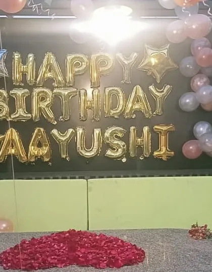 A close-up of the personalized 'Happy Birthday Aayushi' foil balloon arrangement on a rooftop, creating a perfect backdrop for birthday photos.
