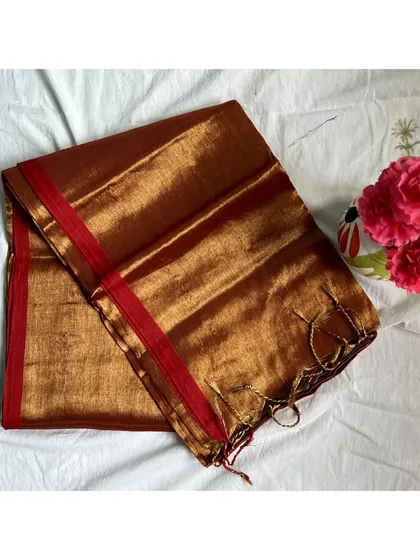 A rich copper-brown tissue cotton saree with a red border. We styled this with a black high-neck blouse for a modern, edgy look.