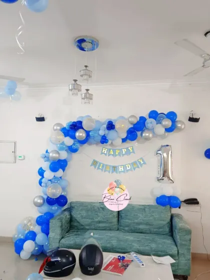 A simple blue, white, and silver balloon arch over a sofa for a first birthday.