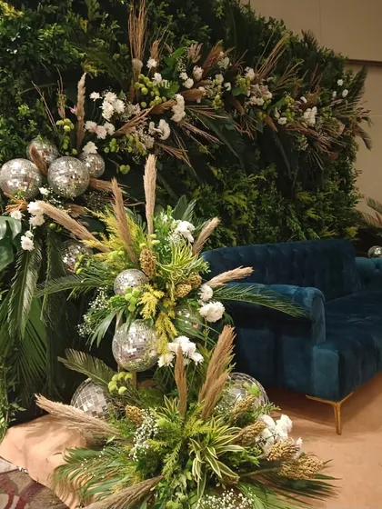 We mix natural and glamorous elements for a unique look. Here, a green wall is accented with pampas grass, white flowers, and sparkling disco balls, creating a 'jungle disco' theme.