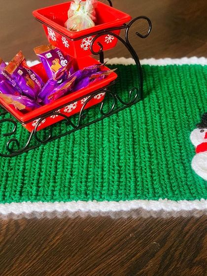 Another view of the green snowman placemat, styled with a decorative sleigh. It shows how you can use these mats as a base for centerpieces too.