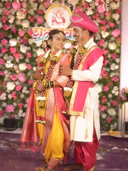 A happy portrait of the newly married couple against a floral backdrop, showcasing their complementary outfits and radiant smiles.