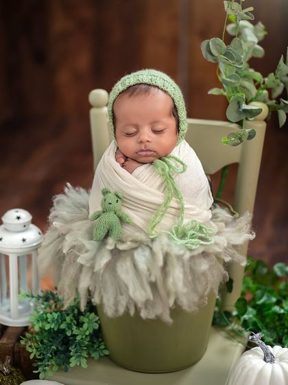 Fresh from a garden of dreams. This little one is posed in a sage green pot with a matching bonnet, surrounded by lush greenery for an earthy, natural feel.
