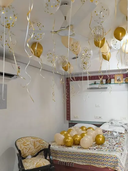 A full room decoration for a welcome home surprise. The ceiling is filled with gold and confetti helium balloons, with more balloons scattered on the bed.