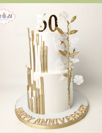 A stunning two-tiered cake for a 50th golden anniversary. The design is modern and elegant, with abstract gold lines and a delicate branch of white and gold sugar flowers.