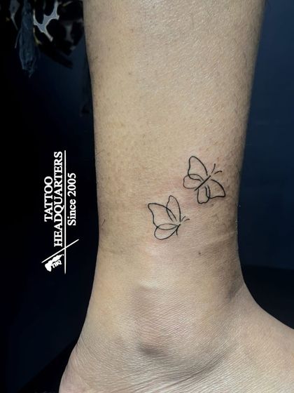 Two tiny, fine-line butterflies tattooed on the ankle, giving the appearance of being in mid-flight.