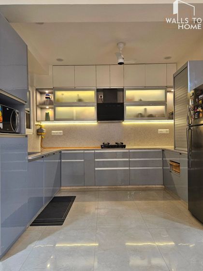 A full view of a U-shaped modular kitchen in a calming grey color. The design includes frosted glass cabinets with internal lighting, providing both storage and a beautiful display area.