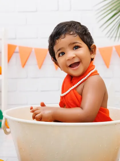A happy baby girl enjoys her orange-themed tub splash after her first birthday cake smash.