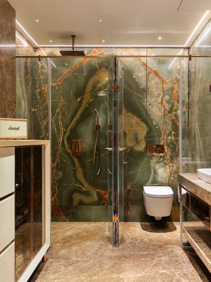 The master bathroom is a statement of pure luxury, with floor-to-ceiling green onyx marble creating a dramatic and artistic effect. The rose gold fixtures and glass shower doors add to the opulent feel.