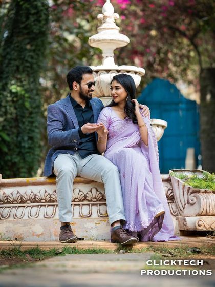 A relaxed and conversational moment between a couple sitting on a garden fountain, dressed in stylish casual and traditional wear.
