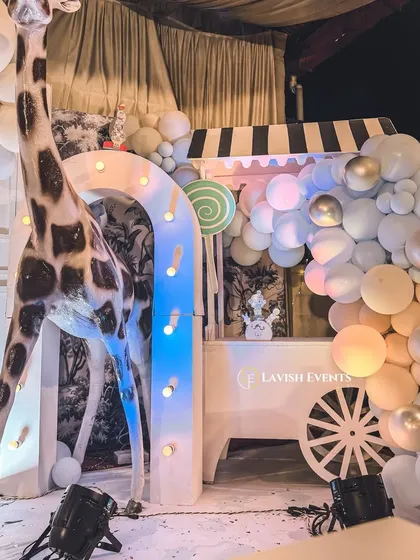 A life-sized giraffe prop stands next to a custom-built candy cart, adding a touch of whimsy and scale to this carnival setup.