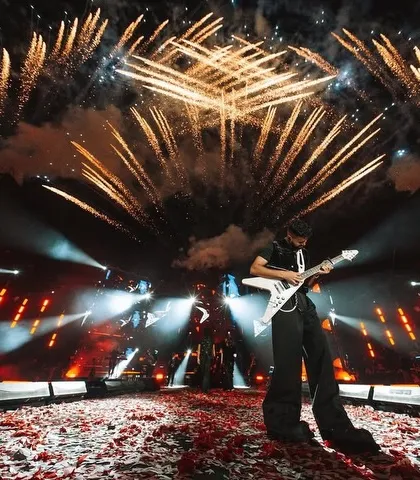 A rockstar moment. AP Dhillon shreds on his guitar on a stage covered in confetti, with fireworks exploding behind him.