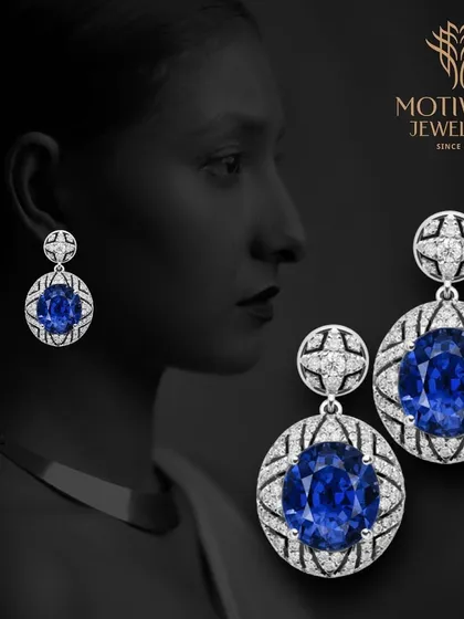 A pair of stunning drop earrings featuring large oval-cut blue sapphires surrounded by a halo of diamonds. A classic and regal design.