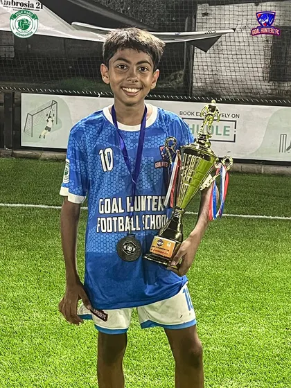 A smiling U-13 player with his medal and the team's trophy.