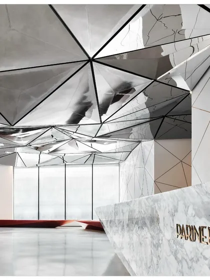 The reflection of the reception desk in the ceiling creates a sense of continuity and visual complexity. The design plays with perception and reality.