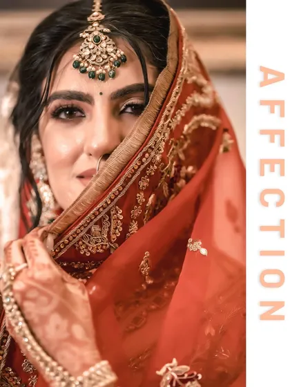 A close-up of the bride, Vanaja, peeking from behind her dupatta, her eyes full of affection and a hint of playfulness.