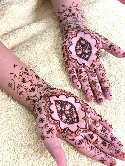 A side view of the completed bridal henna with the central leaf motif. The design extends up the arm with a swirling vine pattern.
