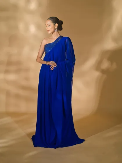A full-length shot of a one-shoulder blue gown from Nikhil Thampi's collection. The elegant pose and soft lighting emphasize the graceful drape and flow of the fabric.