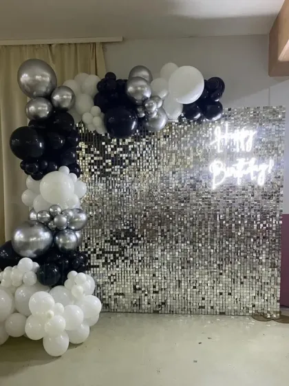 A classic black, white, and silver balloon arch against a sequin backdrop with a neon sign.
