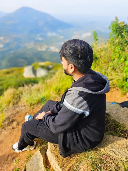 A moment of quiet reflection. A trekker gazes at the distant Nandi Hills from the peak of Skandagiri.