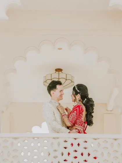 A beautiful, high-key portrait of a cross-cultural couple on a balcony, showcasing their elegant wedding attire and the love between them.