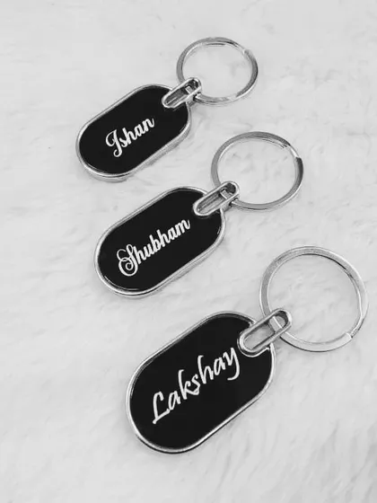 A set of three sleek, oval-shaped metal keychains, each personalized with a different name in a stylish script font.