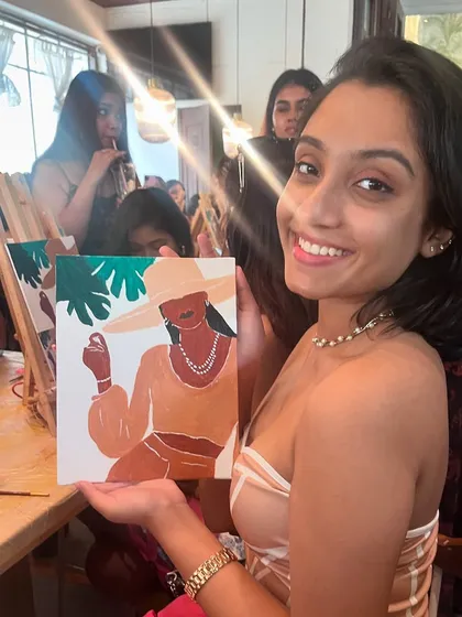 A happy participant showing her finished portrait painting at a cafe workshop. The relaxed environment helps everyone feel comfortable and creative.