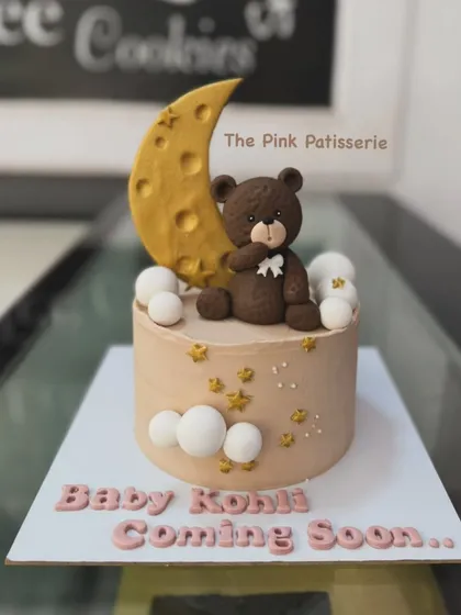 A sweet "Baby Coming Soon" cake, perfect for a baby shower. The design features a teddy bear sitting on a crescent moon.