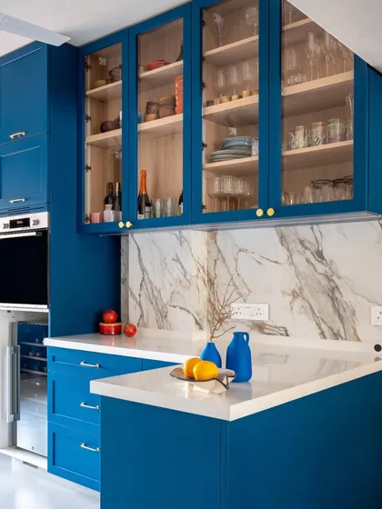 This custom-designed blue kitchen is both functional and a work of art. We paired the bold cabinetry with a classic marble backsplash and elegant glass-fronted upper cabinets. The open layout ensures it remains connected to the living and dining areas, making it a social hub.