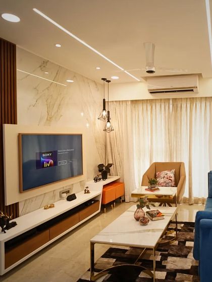 This living room setup shows how we balance different elements. A plush blue sofa, a marble and gold coffee table, and a feature wall with wooden fluting and marble create a look that is modern, luxurious, and well-balanced.