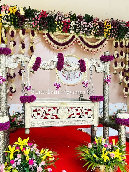 A beautifully decorated silver cradle with purple and white floral arrangements. This setup is perfect for a modern naming ceremony, combining elegance with traditional elements.
