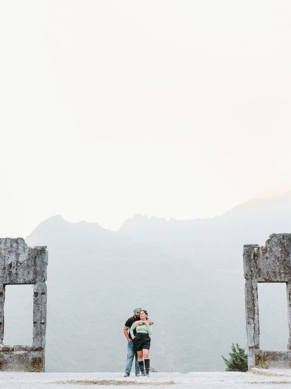 A wide shot showing the couple framed by ancient ruins against the vast mountain range, creating a sense of timelessness and adventure.